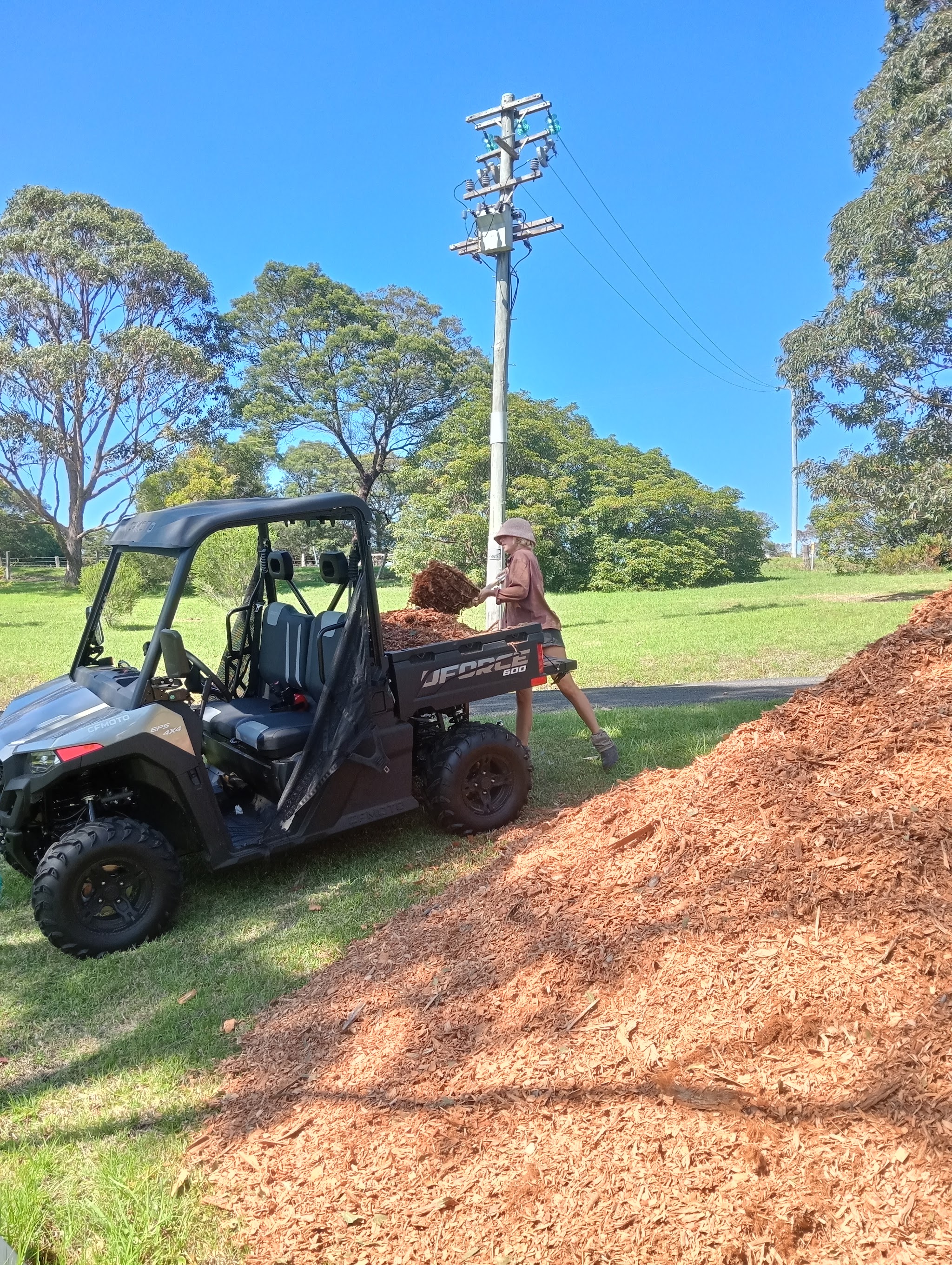 Hatty unloading bark mulch from the back of the work buggy beside a large mulch pile on a rural block